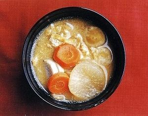 黒いお椀に盛られた大根やニンジンがたくさん入った雑煮の写真