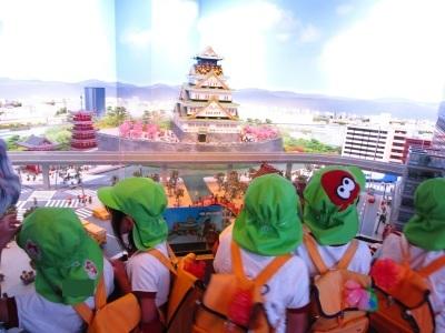 黄緑色の帽子にリュックを背負った子供たちがレゴで作られた大阪城を見ている写真
