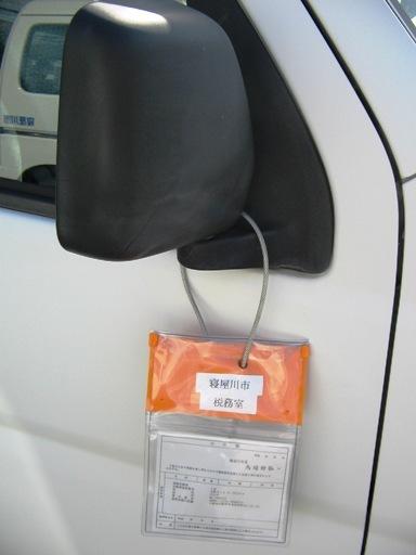 車のミラーにオレンジ色で透明の公示書が入った袋が掛けられている写真