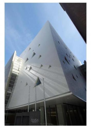 白い壁に三角形のくり抜き模様のある四角い建物のアルカスホールの外観写真