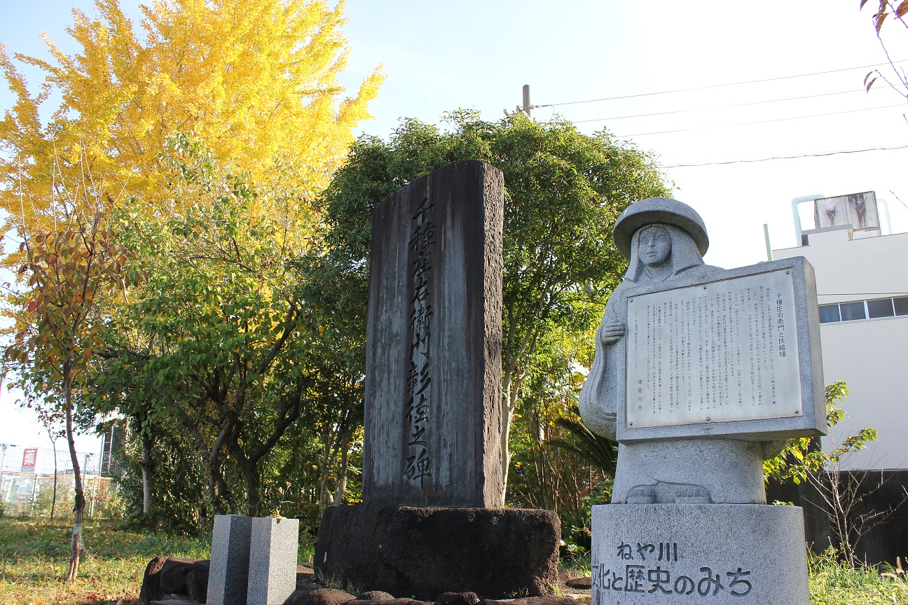 千種庄右衛門の碑の隣に鉢かつぎ姫の形をした石像が説明看板を持っている場所を撮影した写真