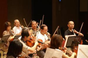 楽譜を見ながらバイオリンなど楽器を演奏する寝屋川市民管弦楽団の写真