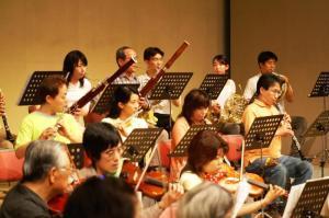 楽譜を見ながらバイオリン、クラリネット、ホルンなどで演奏する寝屋川市民管弦楽団の写真
