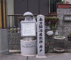 「秦刀鍛冶屋敷跡・井戸」と記された石碑の隣に鉢かつぎ姫の形をした石像が説明看板を持っている写真