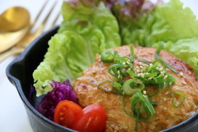 レタスやトマトと色とりどりの野菜と一緒に盛り付けされている鶏ひき肉ともやしの照焼きハンバーグの写真