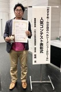 人気コンテスト表彰式で優秀賞を取った山本さんが表彰状と楯を持っている写真
