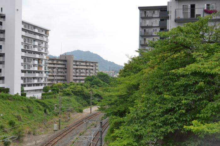 線路の両脇に高層階のマンションが立ち並び、奥に飯盛山が小さく見えている今の写真