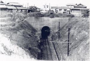 トンネルに続く線路とトンネルの上に家が並んでいる白黒写真