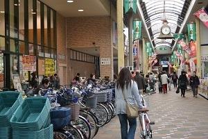 スーパーマーケット外の駐輪場に停めてある自転車や入り口付近に置かれた買い物かご、商店街に訪れた買い物客の写真
