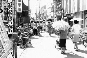 店や映画館などが立ち並ぶ商店街を傘を差して歩いている人々の白黒写真