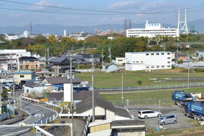 左側には住宅街が広がり右側に田んぼがひっそりと残っており、田んぼの奥には白い建物の大阪病院が写っている現在の寝屋川公園方面の写真