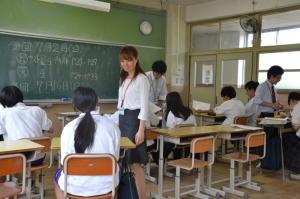 生徒が教室の席に座り学習しており、生徒の席の前に立ち教えている2名の男性や、髪の毛を束ねている女生徒と話をしている女性の教師の写真