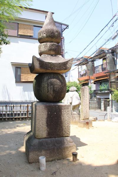 砂の広場に伝秦河勝墓が建てられ後方には住宅が建ち並んでいる写真