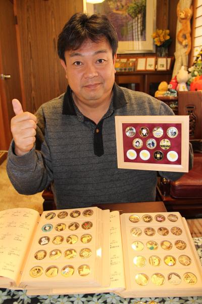 記念メダルがアルバム集ファイルに収められ、盾に入っているメダルを持っている嶋谷徹さんの写真