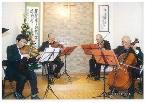 譜面台に置いてある楽譜を見ながらバイオリンやチェロを演奏している4名の男性の写真