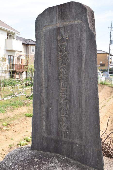 野菜が植えられている畑の前に山口誠太郎君功労碑と記された石碑が建てられ後方に住宅が写っている写真