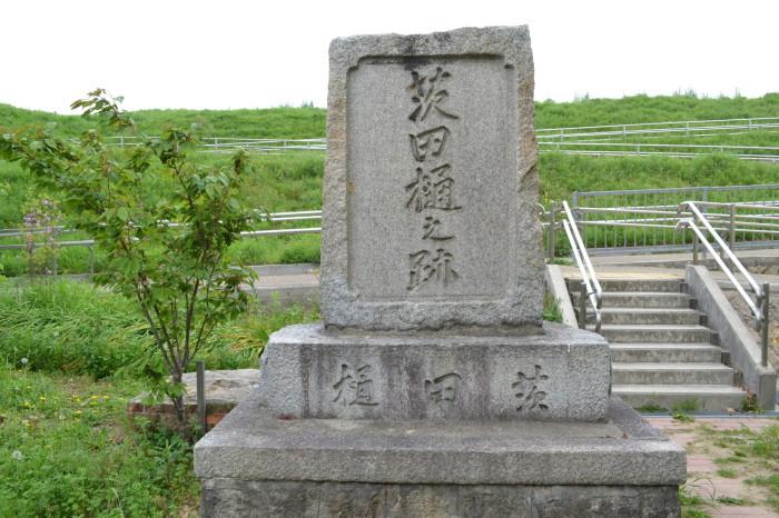 茨田樋之跡碑が建てられており、後方には草が茂っている堤防が写っている写真