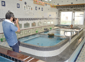 湯舟に浸かっている男性の方にカメラのレンズを向けている松本さんの写真