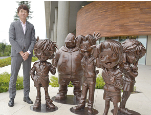 少年探偵団の銅像の横に立っている浅井さんの写真