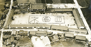 木造の校舎に囲まれた運動場に子供たちが校章と「ネ西」を人文字で書いている航空写真