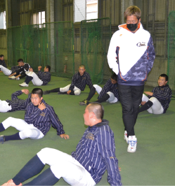 室内練習場にて準備運動をしている生徒たちを見守っている西田直斗さんの写真