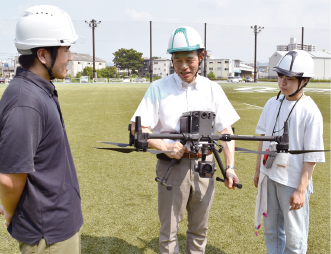 大学のグラウンドで学生と ドローンの実験を行う片田さん（中央）
