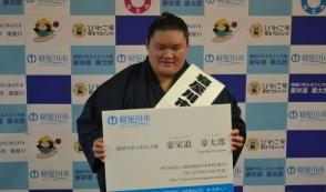 ふるさと大使に選ばれ拡大した名刺を胸のあたりに持っている豪栄道豪太郎関の写真