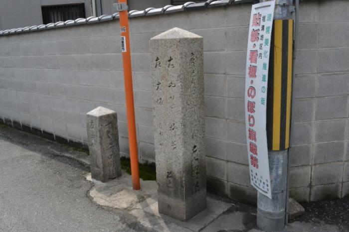 道沿いにあるブロック塀、カーブミラーの両脇にある道標、「貼紙、看板、のぼり旗厳禁」と書かれた看板が設置された電柱の写真