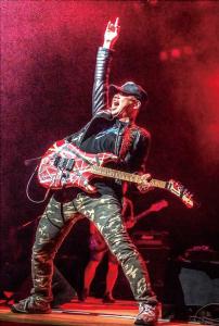 ギターを持ち左手を上に上げている米田 喜一さんに赤いライトが当たっている写真