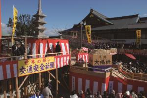 紅白の横断幕で飾られた成田山不動尊のやぐらの下に大勢の人々が集まっている写真