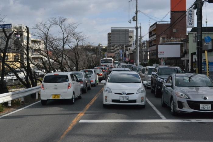 道路で車が信号待ちをしており、道路沿いにはマンションなどが建ち並んでいる写真