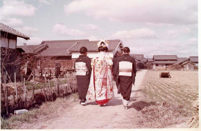 農道を花嫁姿の女性と着物姿の女性2名が横一列に並んでおり、その前を着物姿の男性が歩いている写真