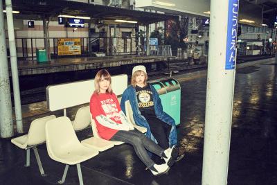 ガールズロックバンド（yonige）の2名の女性が駅のホームのベンチに座っている写真