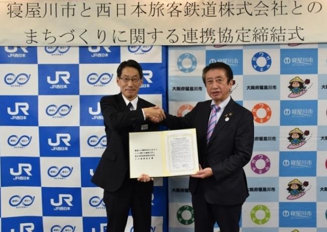 西日本旅客鉄道株式会社の川井正支社長と市長が協定書を持ち、握手している写真