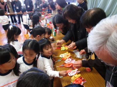 子どもたちが、テーブルの上にあるペープサートに貼るシールを大人たちからもらおうとしている写真