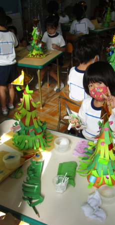 テーブルの上で折り紙を使ってクリスマスツリーを飾る子供たちの写真