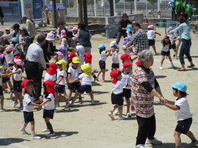 園庭で大人たちとダンスをする子供たちの写真