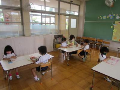 教室でテーブルごとに分かれて本を見ている子供たちとエプロン姿の先生が子供たちに教えている写真