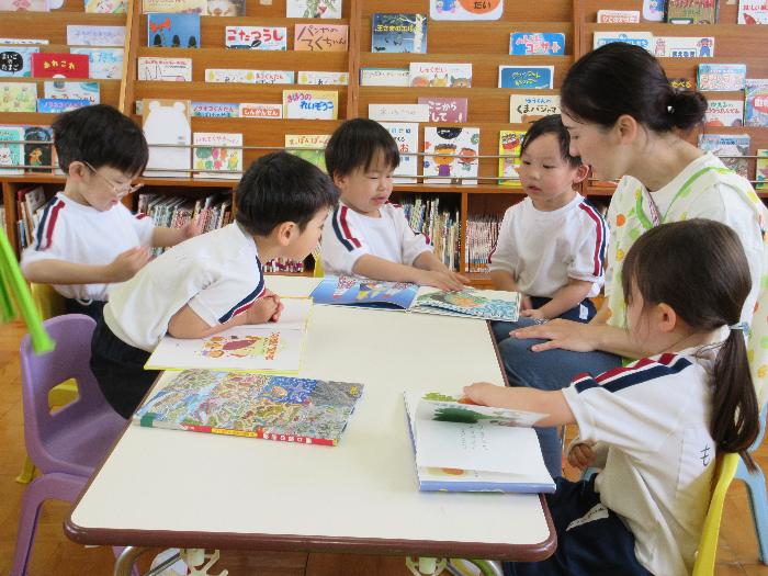 先生が椅子に座っている子供たちと一緒に絵本を見ている写真