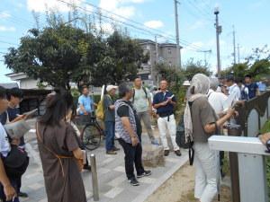 大きな木が生えている遊歩道に集まって説明を聞いている参加者の写真