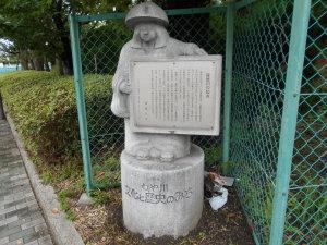 「ねや川文化と歴史のみち」と書かれた台座の上に立って看板を持っている石像の写真