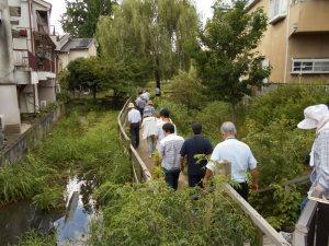 雑草や木が生い茂った水路沿いの遊歩道を歩いている参加者の写真