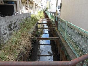 周囲の建物と塀やフェンスで区切られている用水路の写真