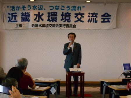 近畿水環境交流会と書かれた幕が貼られた前で、北川市長がマイクを右手に持ち祝辞を延べている写真