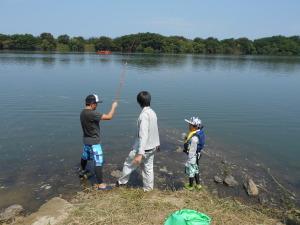 2名の男性と男の子が川岸に立ち、左側の男性が竿を上げている写真