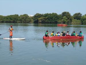 赤色のEボートに乗る体験を行っている参加者が乗っており、左側には白色のＳＵＰ（スタンドアップパドルボード）に立って乗っている人の写真