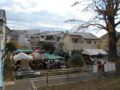 並んで建つ家の間の公園内に青、緑、ピンクのテントが設置され、茨田イチョウまつり会場全景写真