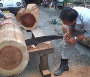 大きなのこぎりを使いスギ原木を加工している男性の写真