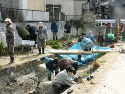 小川の土手に、スコップで土を掘りウンリュウヤナギを植え付けている参加者の写真