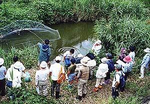 府立工専の河に投げ網を行っている男性とその様子を周りで見ている参加者の写真